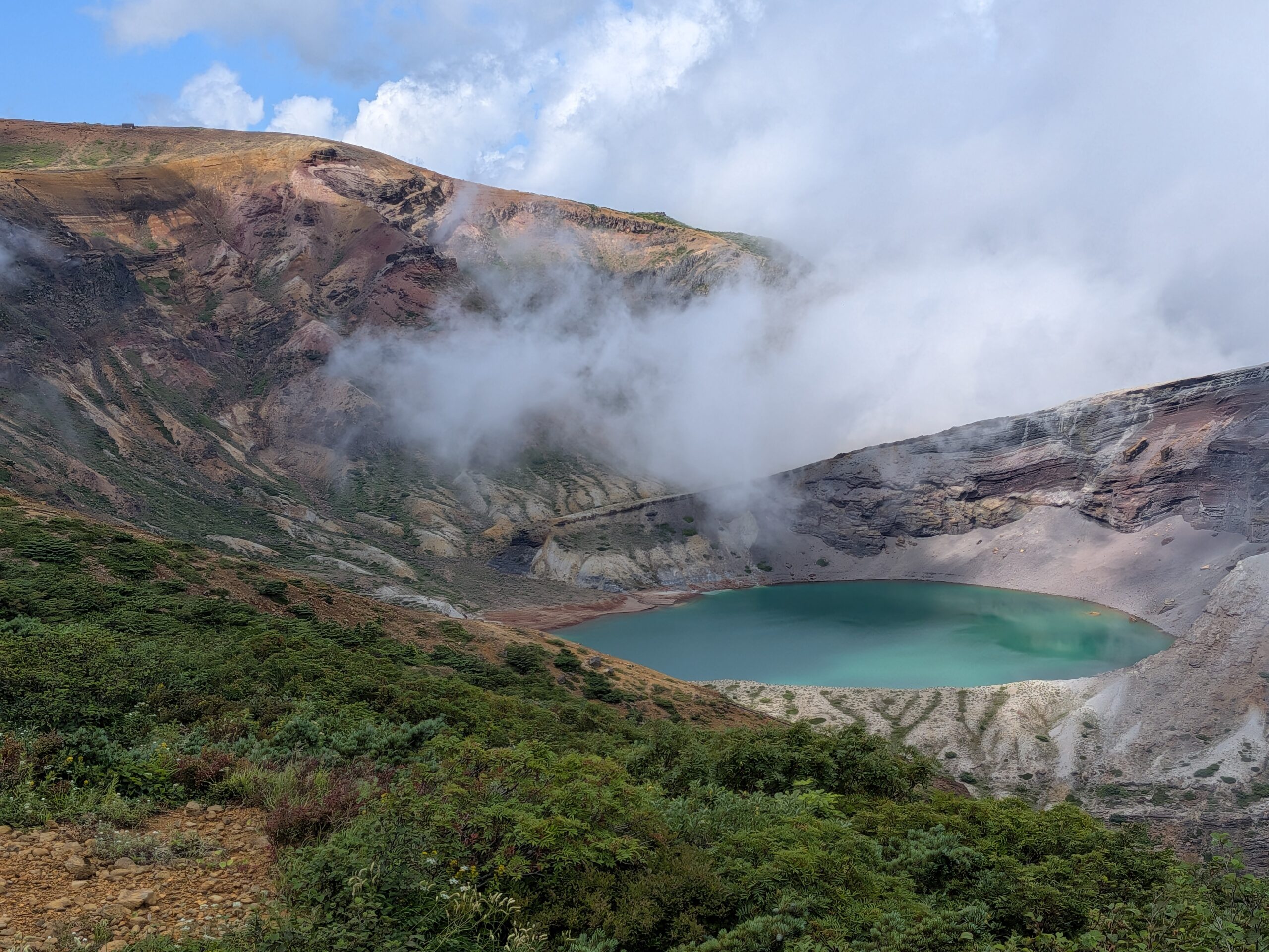 蔵王の御釜の火口湖と雲がかかる山肌